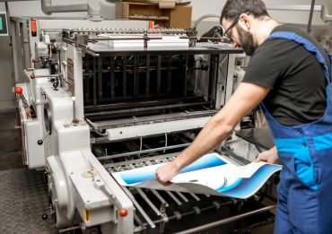 Typographer checking printing quality standing near the old press machine at the printing manufacturing